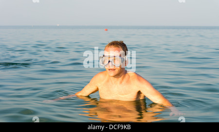 Man wearing goggles swimming in the sea standing chest high in the saltwater in the summer sun while enjoying his vacation Stock Photo