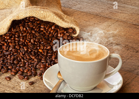 Coffee and Sack of Coffee Beans - a cup of hot steaming espresso coffee on a rustic plank background, with a sack of coffee... Stock Photo