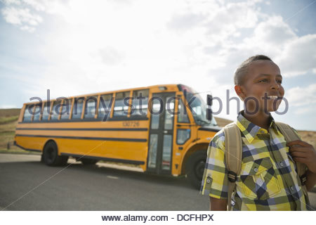 Smiling schoolboy standing near school bus