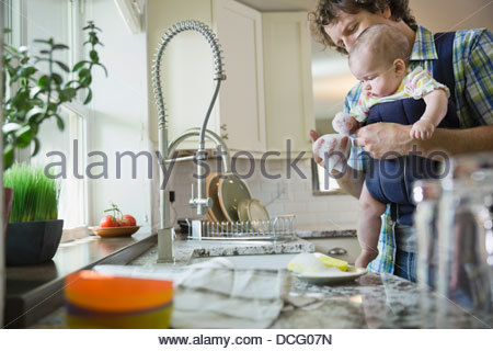 Father holding baby girl while washing dishes