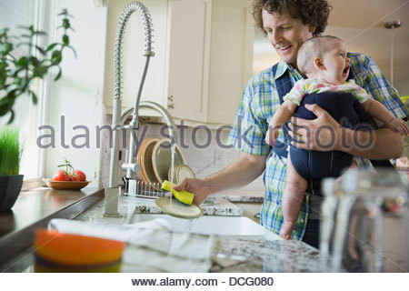 Father washing dishes while carrying baby girl Father washing dishes while carrying baby girl