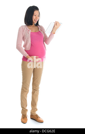 Full body six months pregnant Asian woman using digital computer tablet pc standing isolated on white background. Stock Photo
