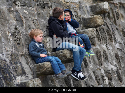 Lyme Regis, UK 17 August 2013. Tourists brave the wet weather. Three boys sitting on stone steps of the Cobb Cob harbour wall. Credit:  Carolyn Jenkins/Alamy Live News Stock Photo