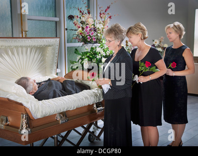 Three Women Standing By A Man's Body Laying In A Coffin Stock Photo