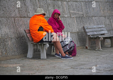 Lyme Regis, UK 17 August 2013. Tourists brave the wet weather. Couple in brightly coloured jackets sitting on bench by the Cobb Cob harbour wall. Credit:  Carolyn Jenkins/Alamy Live News Stock Photo