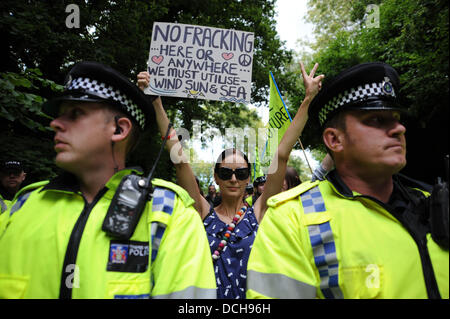 Balcombe, West Sussex, UK. 18th August 2013.  A young woman holds up a poster behind police line as thousands of protesters converged on Balcombe in West Sussex today to march and protest against the Cuadrilla fracking site in the village .  Photograph taken by Simon Dack/Alamy Live News Stock Photo