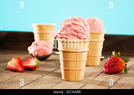 strawberry ice cream in waffle cones on wood with a scoop in background Stock Photo