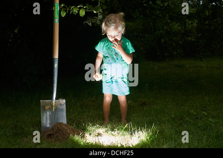 Child blond baby girl stands and digging for lighting hole in the ground Stock Photo