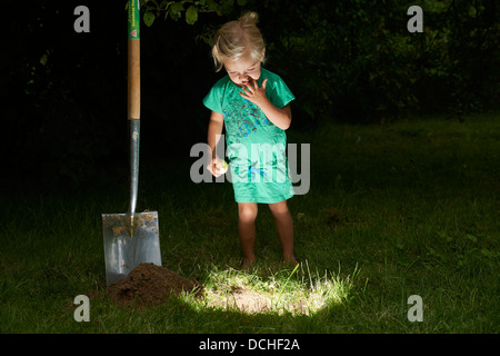 Child blond baby girl stands and digging for lighting hole in the ground Stock Photo