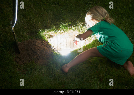 Child blond baby girl stands and digging for lighting hole in the ground Stock Photo