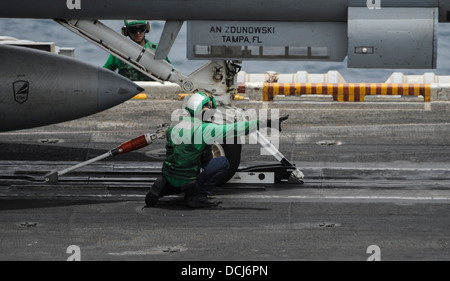An aviation boatswain's mate (equipment) checks the catapult as an F/A-18F Super Hornet assigned to the Black Knights of Strike Stock Photo