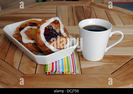 Original Danish pastry of laminated yeast-leavened dough - flaky and delicate crust and a mug of coffee on a café table. Stock Photo