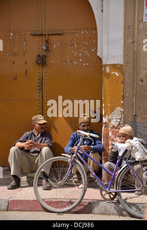 Three men and a bike situated in front of traditional shaped gates.  The old walled city of Taroudant,  Morocco, North Africa. Stock Photo