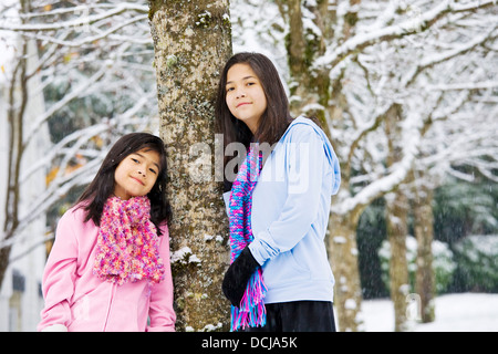 Two little girls standing by tree in fresh snow Stock Photo