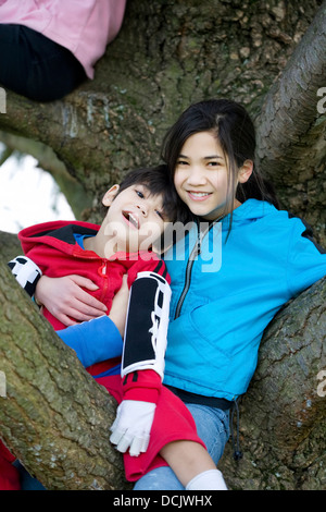 Sister holding disabled brother in tree Stock Photo