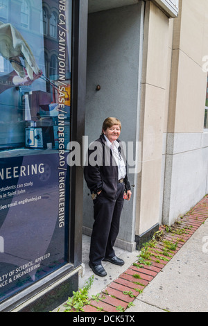 A female security guard at the University of New Brunswick in St John, Nova Scotia stands outside in an entryway and smokes. Stock Photo