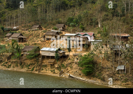 Horizontal view of traditional stilted wooden huts and homes clinging to the banks of the Nam Song river close to Vang Vieng Stock Photo