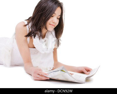 Teen girl in white dress lying down reading a magazine Stock Photo