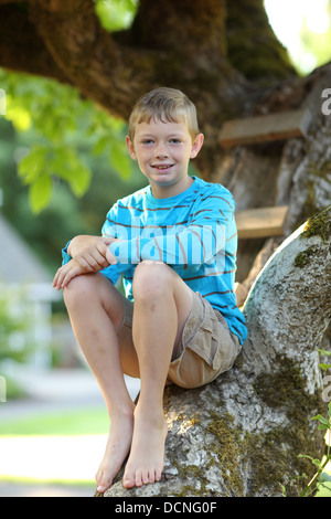 Portrait of young boy sitting in tree Stock Photo