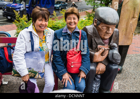 Asian tourists posing with an over-sized, larger than life, group of wooden sculptures in St John, Nova Scotia, Canada. Stock Photo