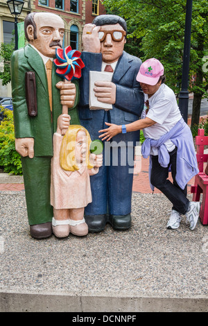 A female Asian tourist posing with an over-sized, larger than life, group of wooden sculptures in St John, Nova Scotia, Canada. Stock Photo