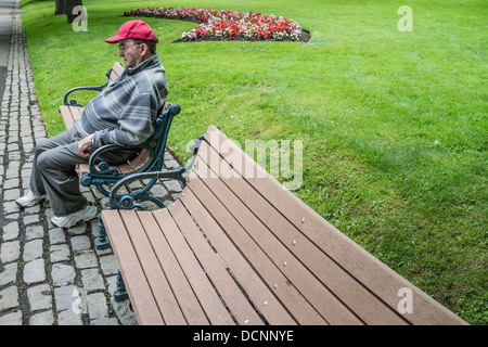 An older Canadian man sits, looking unhappy and deep in thought, on a park bench in King's Square, St. John, Nova Scotia, Canada Stock Photo
