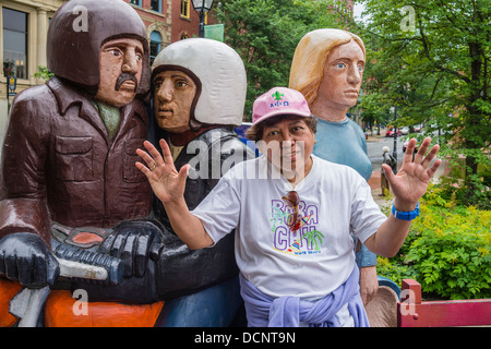 A female Asian tourist posing with an over-sized, larger than life, group of wooden sculptures in St John, Nova Scotia, Canada. Stock Photo