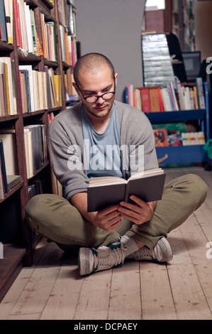 Male college student sitting on floor in library, reading book. Stock Photo