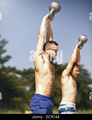 Two strong young men lifting heavy kettlebell weights Stock Photo