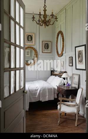 View through open doorway to charming bedroom with wooden wall paneling and French antiques Stock Photo