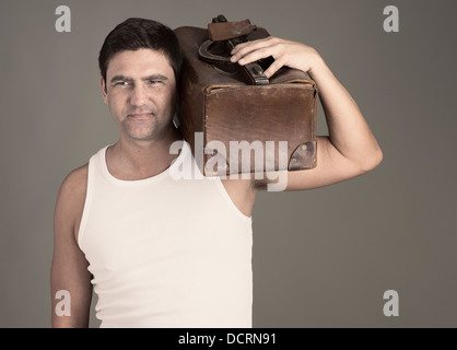 Determined man in white tank top holding brown leather luggage bag on his shoulder Stock Photo