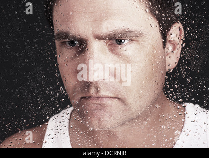 Closeup of pensive man looking through window covered with raindrops Stock Photo