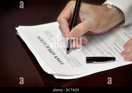 Business man signing loan application with black pen on desk Stock Photo