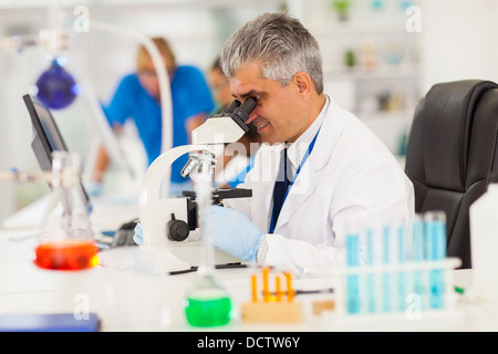 senior medical researcher looking through the microscope with colleagues on background Stock Photo