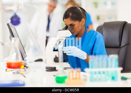 young Indian medical researcher looking through microscope in laboratory Stock Photo