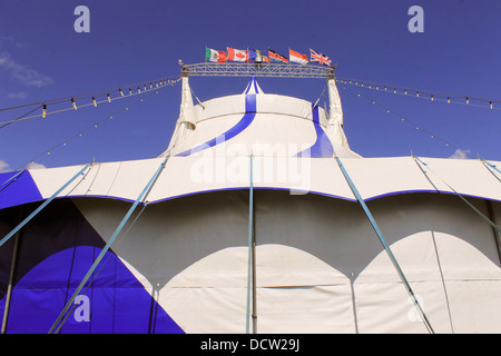 Blue and white circus tent with different country flags, blue sky and cloudscape background. Stock Photo