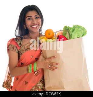 Happy grocery shopper. Portrait of beautiful traditional Indian woman in sari dress holding paper shopping bag full of groceries isolated on white. Stock Photo