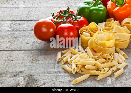 Pasta and Vegetables - raw bronze die pasta and vegetables on a rustic wooden background. Lots of texture. Stock Photo