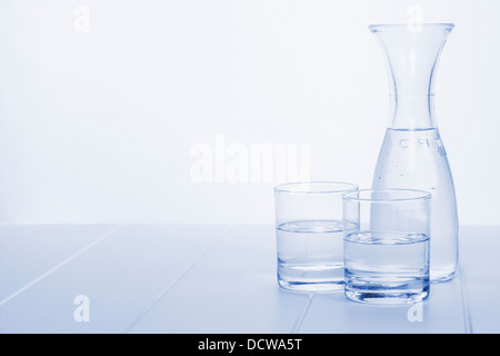 Water Carafe and Two Glasses - a carafe of water on a table with two glasses, blue toned, horizontal. Stock Photo