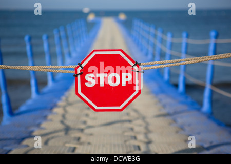 A stop sign bars entry to a pier leading out to the sea Stock Photo