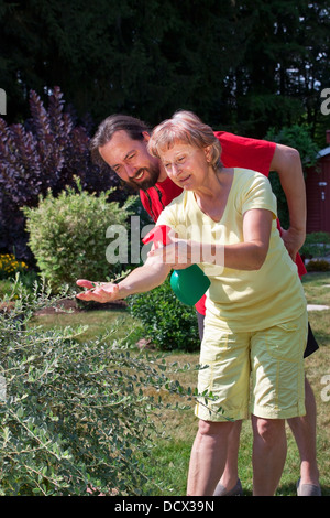 Man watches senior woman at gardening Stock Photo