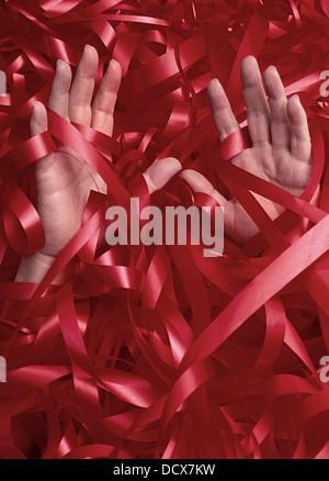 Hands sinking under a mass of bureaucratic red tape concept image Studio England UK Stock Photo