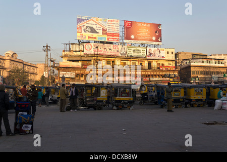 A number of parked auto rickshaws, people and shops outside the Jodhpur train station early in the morning with sun light up Stock Photo