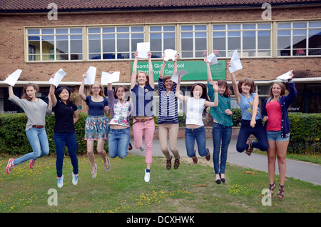 A group of happy students jumping in the air while holding their successful GCE exam results outside their school UK.