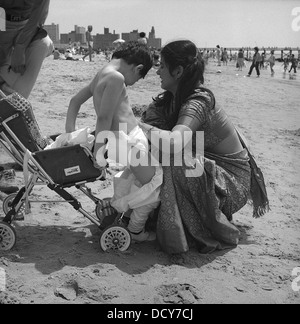 Indian mother changing her son's diapers on the beach of Coney Island Stock Photo