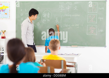 primary schoolboy writing Chinese character on the chalkboard with teacher next to him Stock Photo