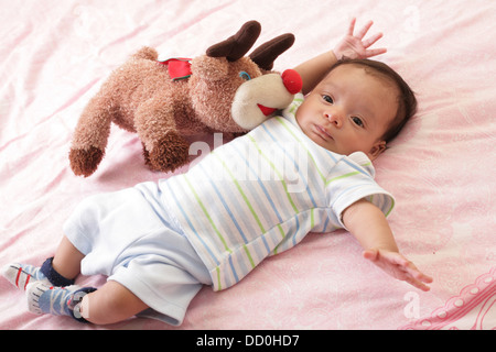 hispanic baby with teddy bear laying on bed Stock Photo