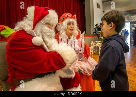 A deaf Hispanic boy communicates with a deaf Santa Claus and Mrs. Santa using sign language Stock Photo
