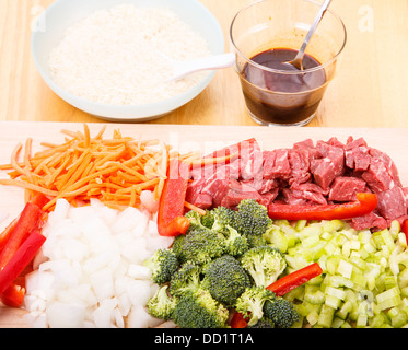 Beef stir-fry ingredients on cutting board with rice and soy sauce in background Stock Photo
