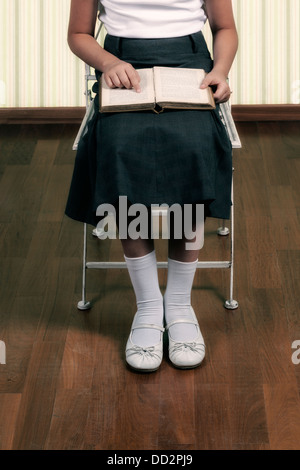 a girl in school uniform sitting on a chair, reading a book Stock Photo